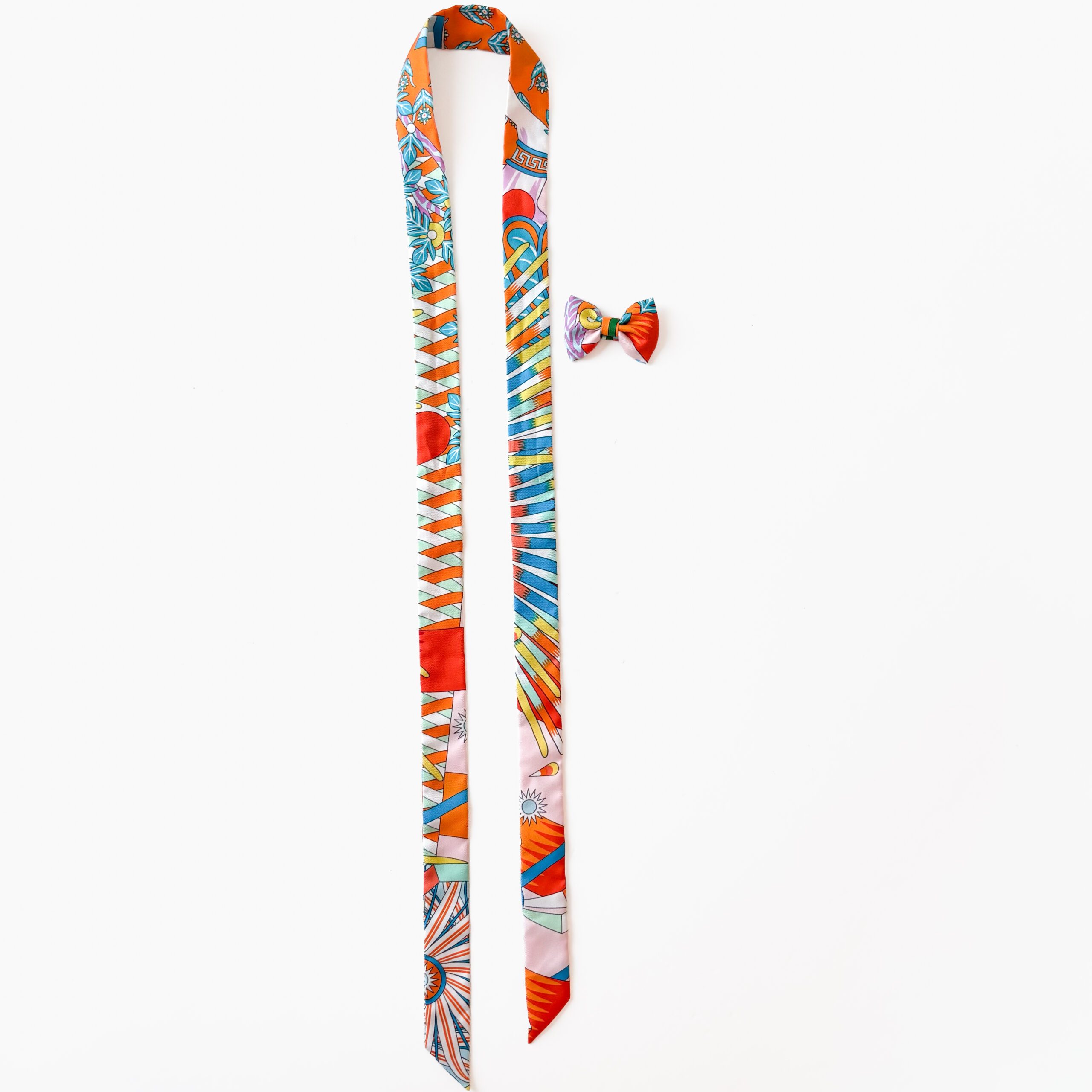 Full view of a colorful orange and blue Hermès silk Twilly scarf and matching mini bow accessory on a white background Hermès Sous le Charme d'Orphée Silk Multicolor Twilly Scarf & Pre-Tied Bow Tie Set - Image 1